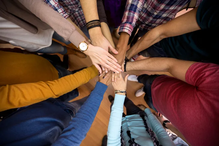 Diverse individuals putting their hands in the center of the circle