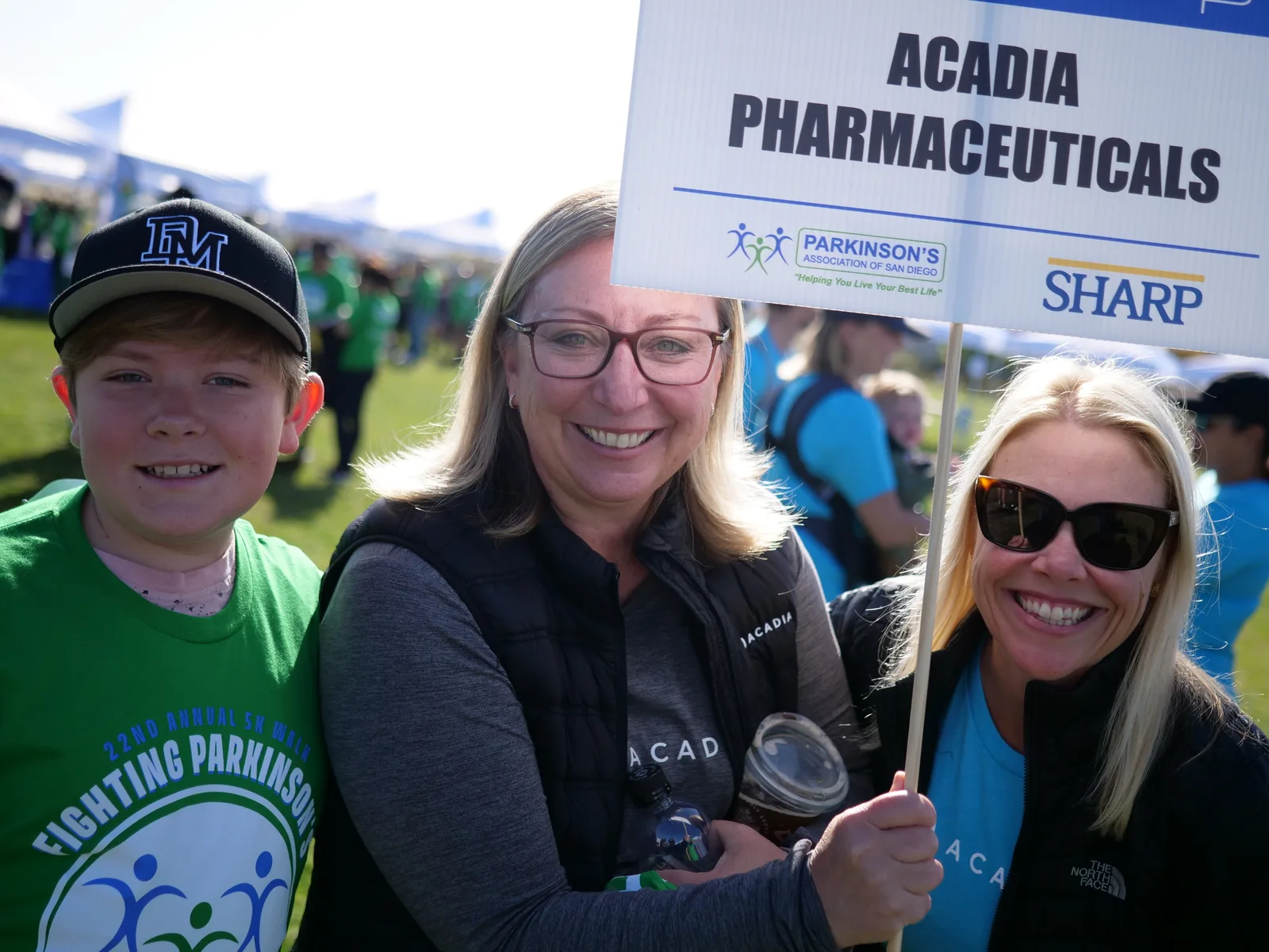 Group photo of Acadia Pharmaceuticals team members at a Parkinson’s Disease awareness event, holding a sign with Parkinson’s Association and Sharp logos