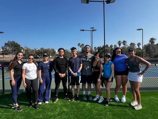 Group of Acadia team members and interns posing together on a tennis court under a clear sky, showcasing teamwork and wellness activities