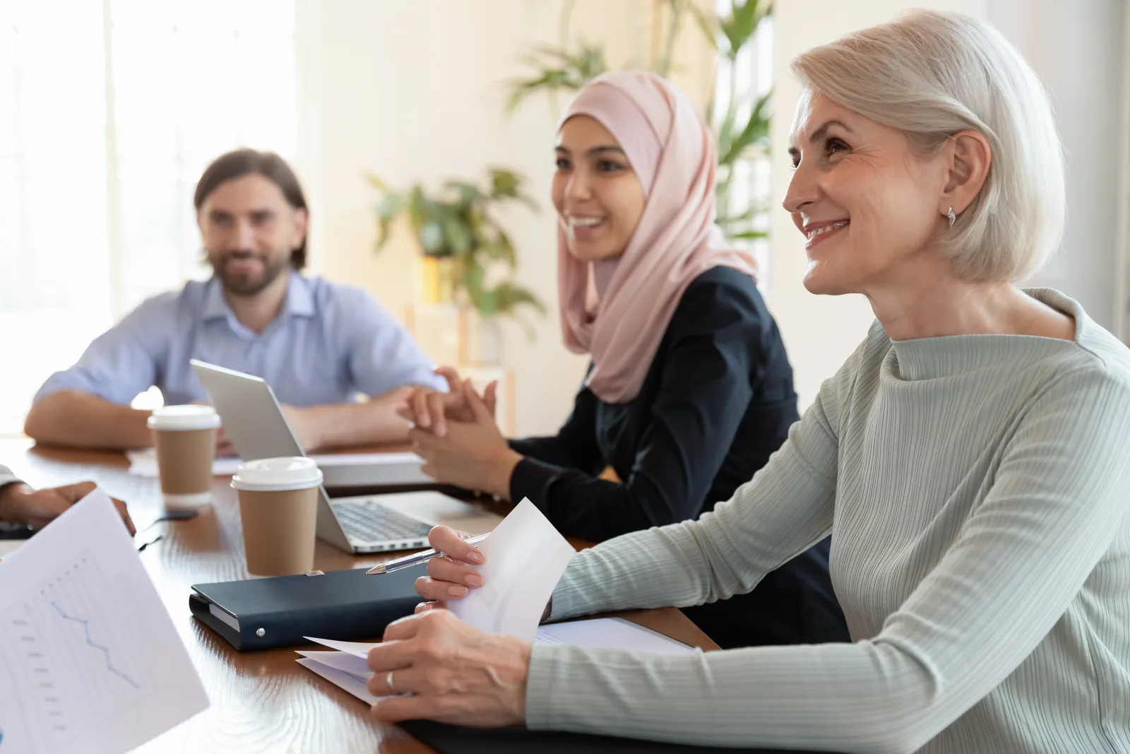 A group of smiling professionals engaging in a business discussion around a conference table, showing diverse cultural backgrounds and teamwork