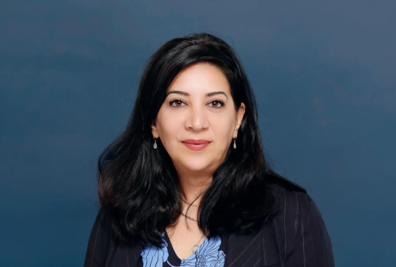 Professional headshot of Chirine Fiouzi with dark hair, wearing a blazer against a blue background