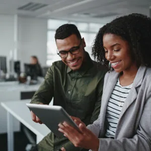 Two colleagues collaborating on a tablet in a modern office setting, representing teamwork and digital innovation