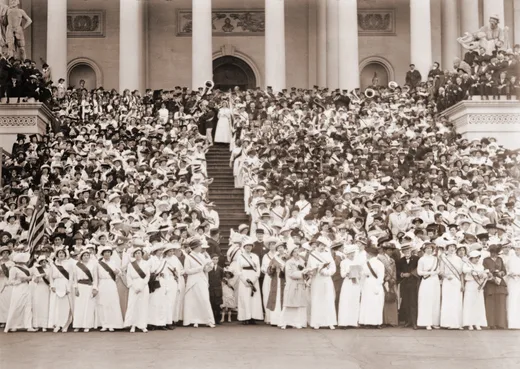 A historic photograph capturing a large crowd of women dressed in white during a suffrage march, symbolizing unity and the fight for women’s voting rights.