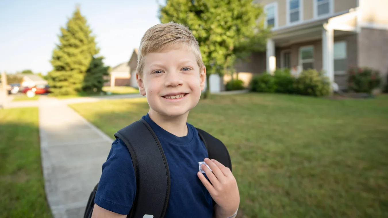 Young boy smiling outdoors with a backpack, representing children impacted by rare diseases, for Rare Disease Day awareness