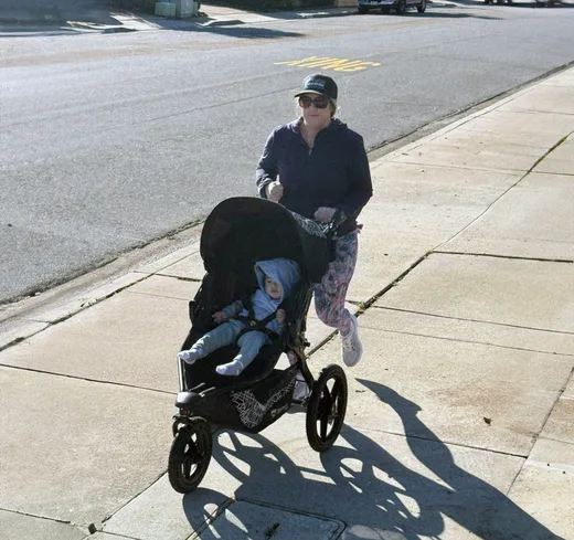 A woman jogging on a sidewalk while pushing a baby stroller, symbolizing active parenting and commitment to health.