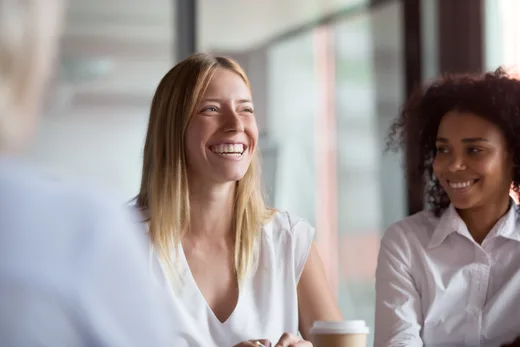 Two professional women sharing a smile during a casual meeting, highlighting a supportive and empowering workplace environment